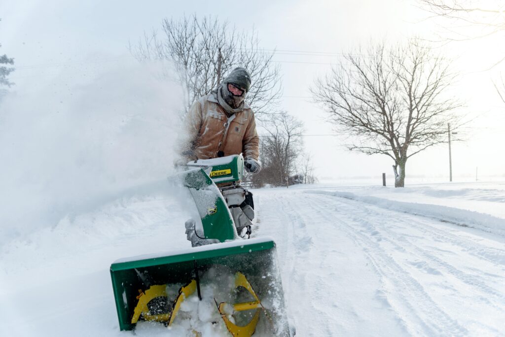 Man using a snow blower to clear snow during winter in Essex, ON under cold weather conditions.